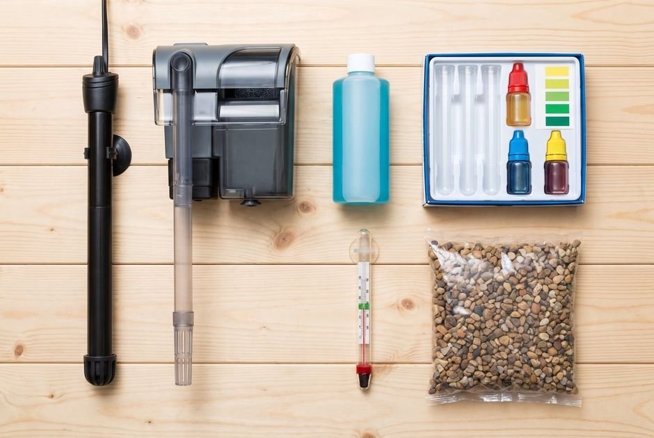 Aquarium starter kit laid out: heater, filter, conditioner, test kit, thermometer, and gravel